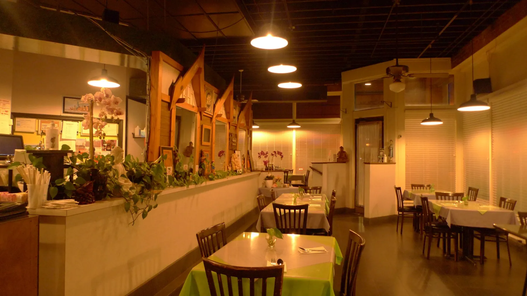 The warmly lit dining room at Bangkok City Restaurant with set tables, plants and wood details