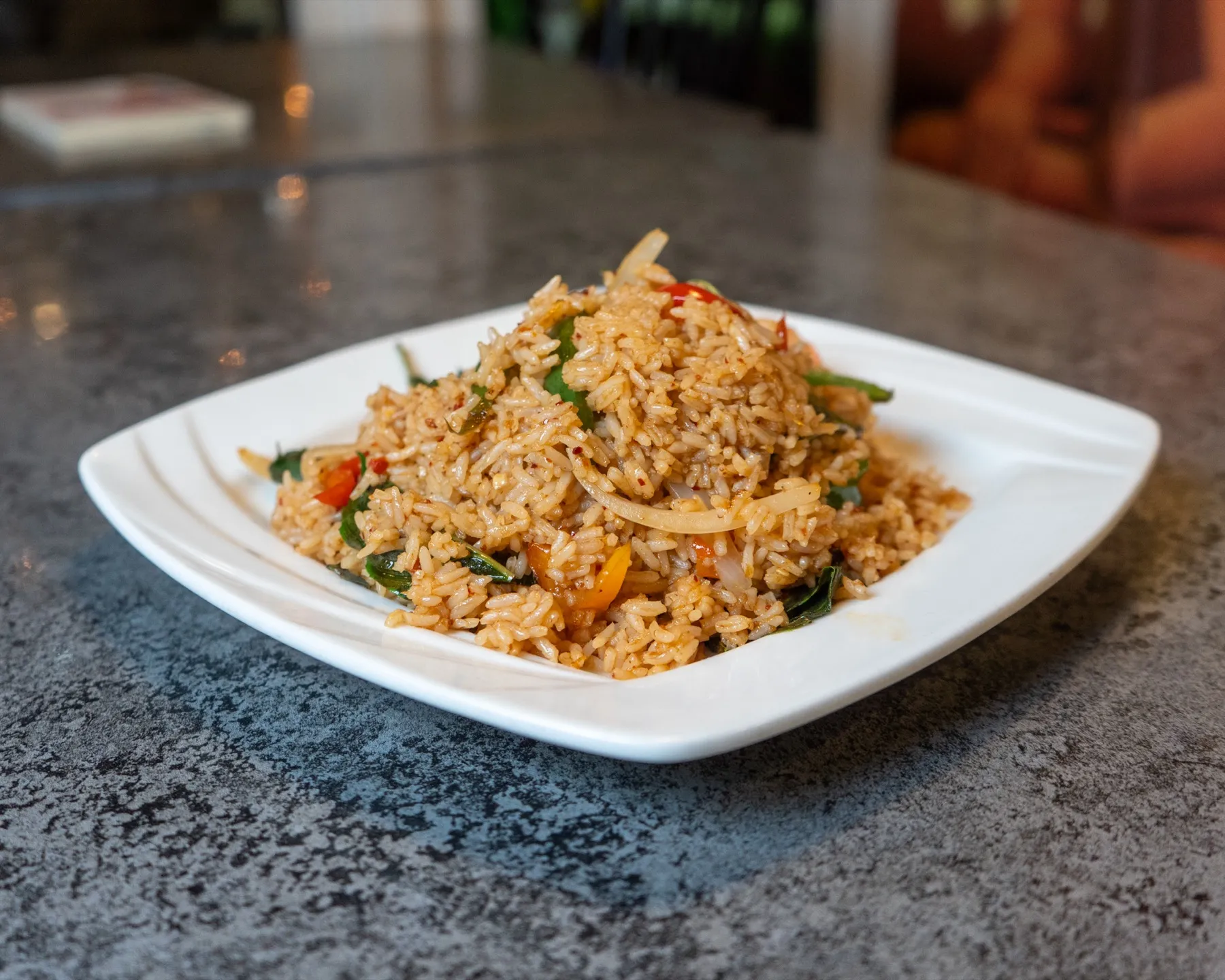 Thai fried rice with basil, onion and colorful peppers on a white plate