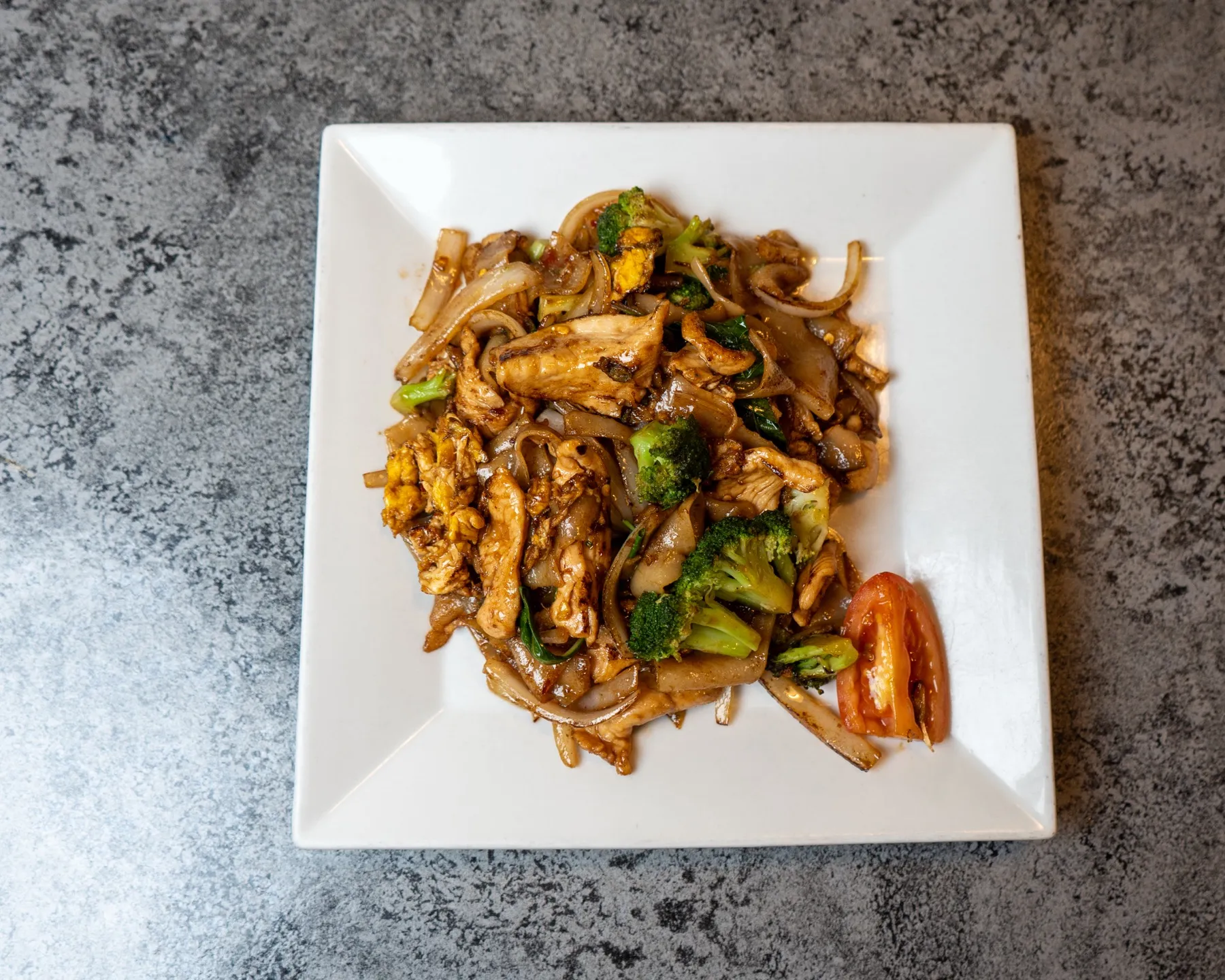 Wide rice noodles stir-fried with chicken, broccoli, onion, egg and tomato