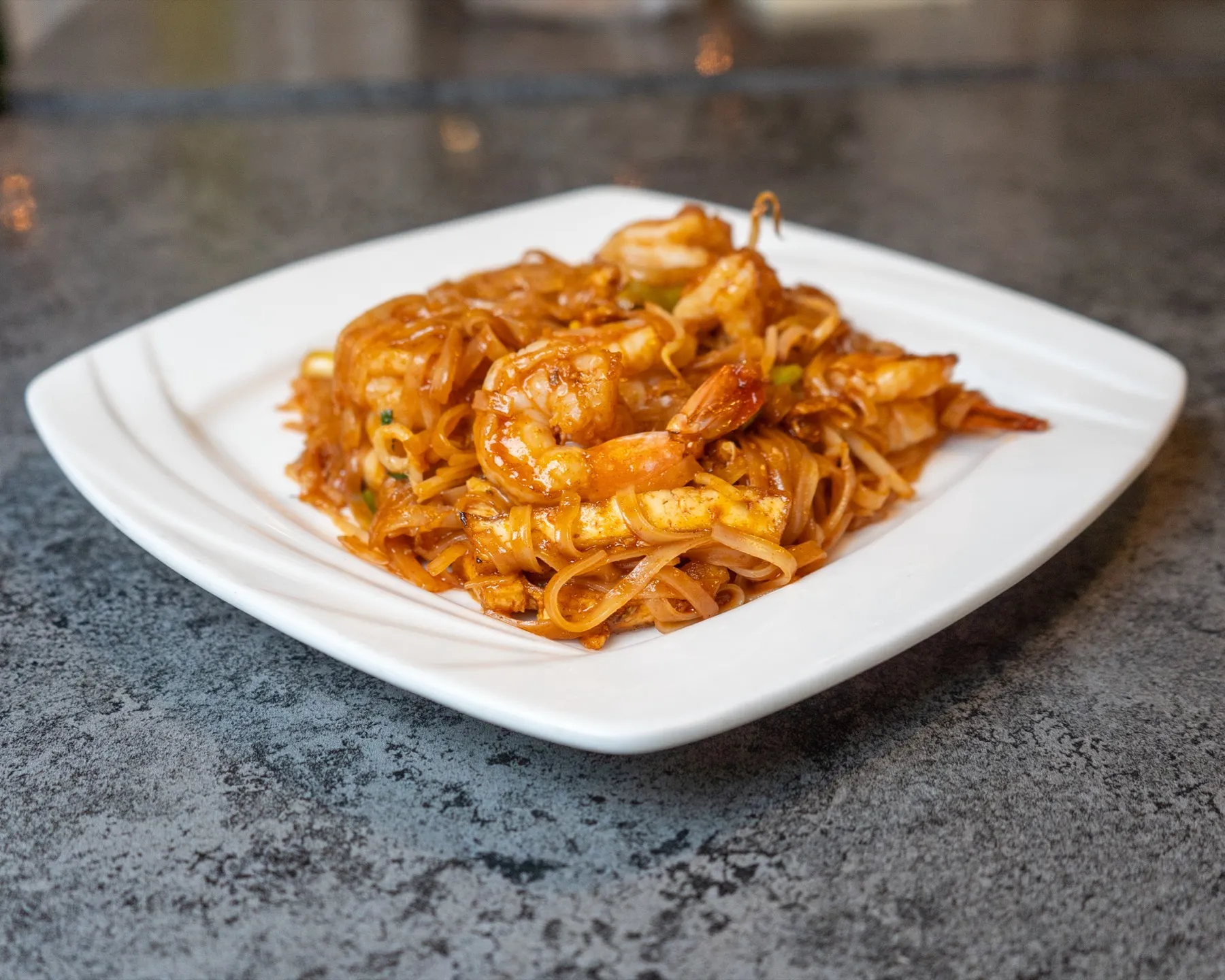 A plate of shrimp Pad Thai with rice noodles, tofu, bean sprouts and green onion